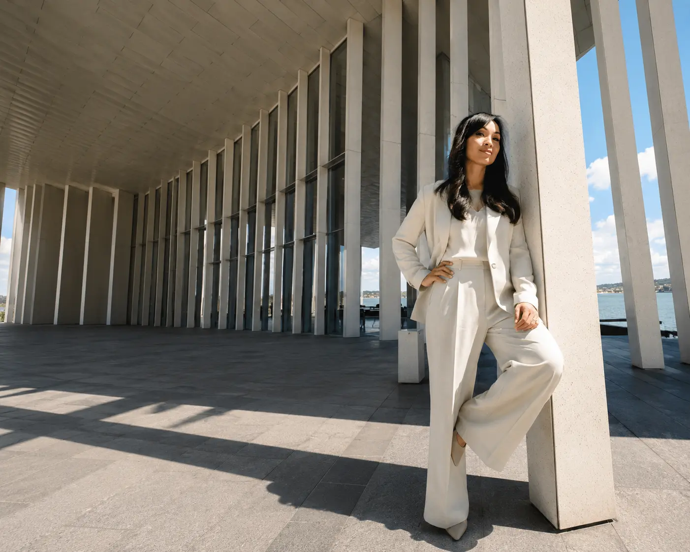 Linh Podetti in a cream suit, leaning against a stone column
